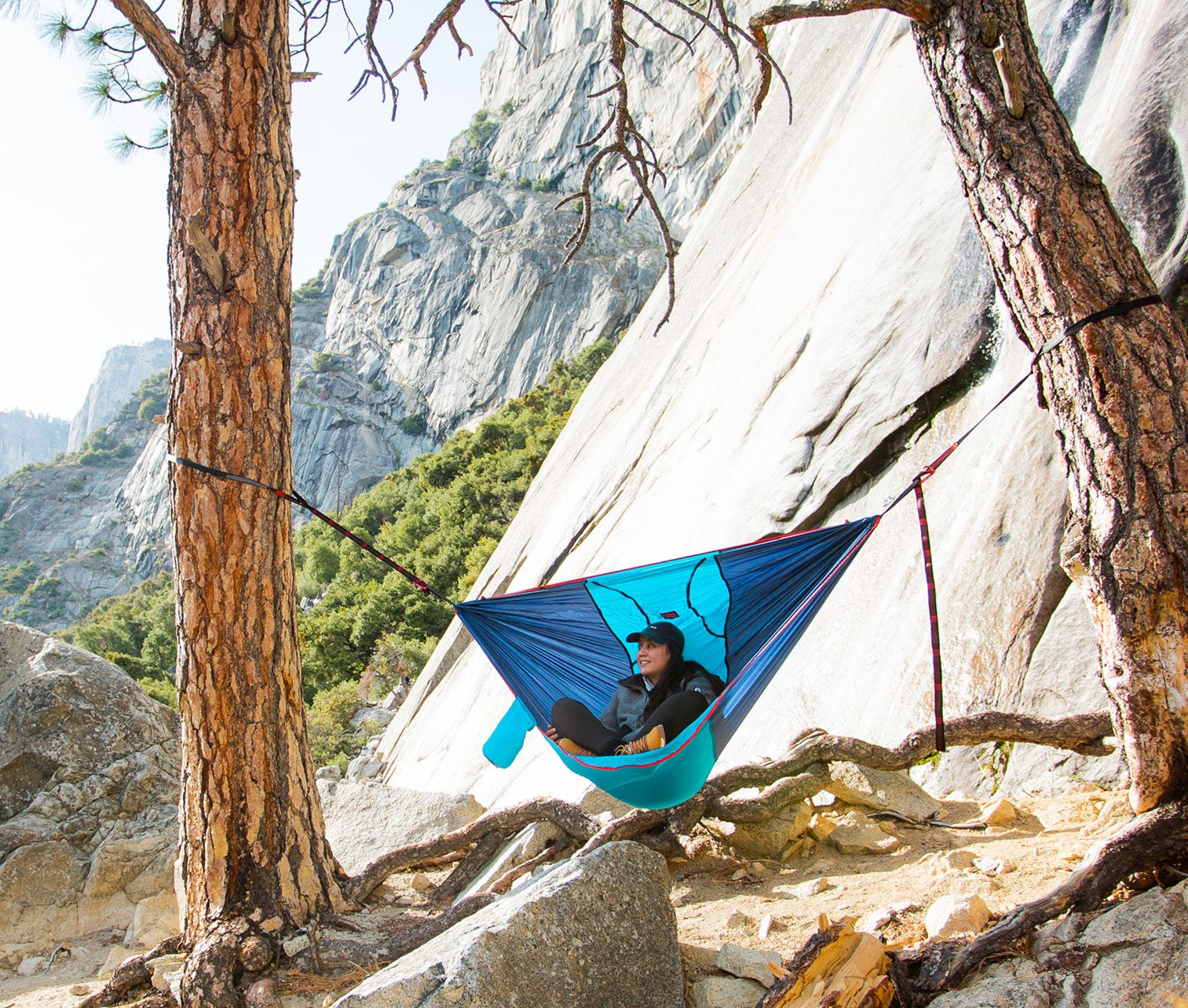 Person in a blue hammock between two trees with a mountainous landscape in the background